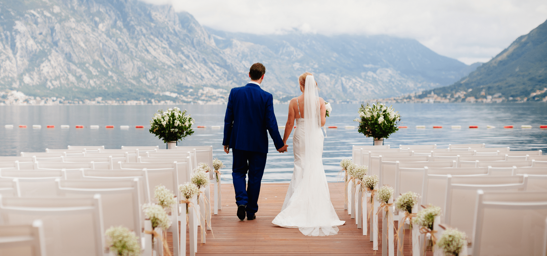 Wedding couple walking down the aisle facing a mountain lake.
